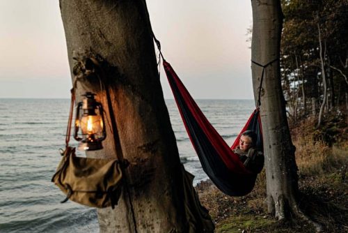 Woman relaxing in a hammock that is tied between two trees next to the sea.