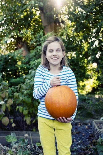 young girl proudly holding a pumpkin she has grown
