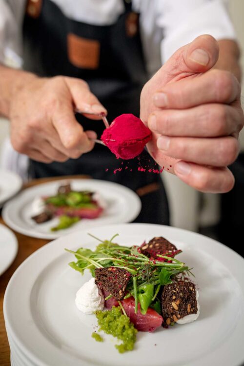 Chef adding some dried beetroot powder to a dish of marinated salmon with samphire.