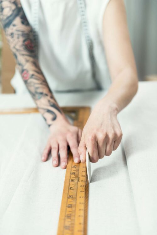 Dressmaker with a sleeve tattoo marking out a pattern on a piece of cloth.