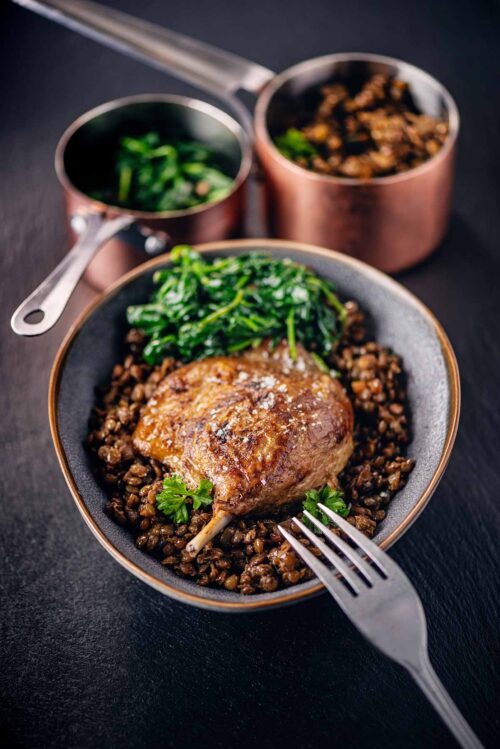 Dish of duck confit with Puy lentils and spinach.