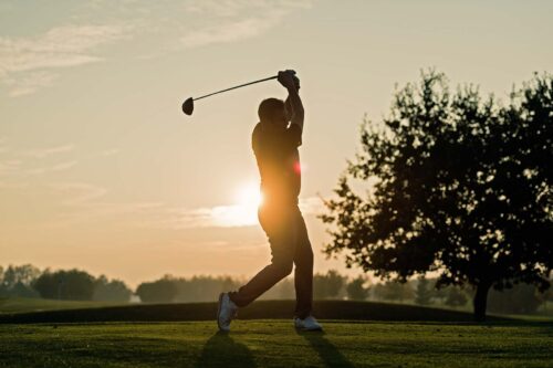 Silhouette of a golfer as he hits a perfect tee shot. Photographed against a setting sun