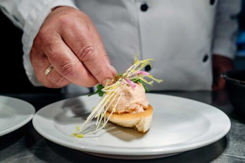 Chef at the pass preparing a dish of salmon mousse made from warm smoked salmon served on toasted bread with fresh young asparagus stalks and decorated with wood sorre