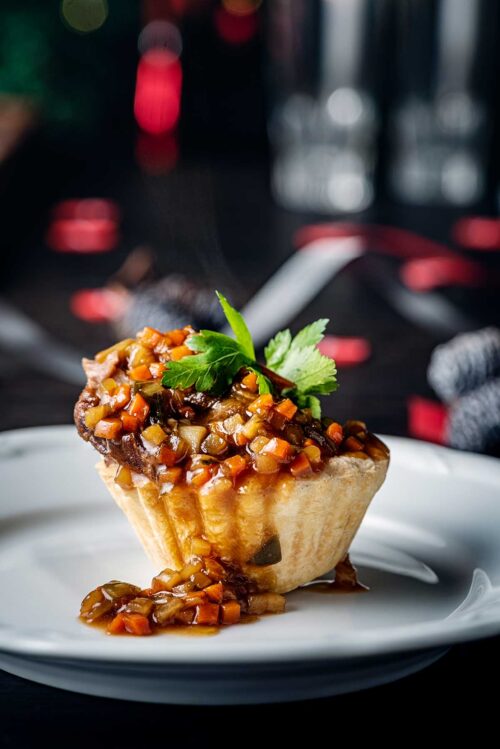 Close-up of a dish of beer marinated pig cheek served in a baked pastry tart with finely chopped carrots, potatoes and onion.