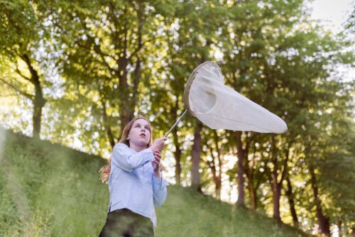 Portrait of young girl holding an insect net and fiercely concentrating on trying to catch some butterflies.