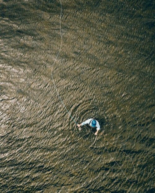 Portrait of a fly fisherman casting out his line from a drone POV.