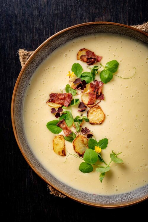 Bowl of leek and potato soup with pea shoots, crisped potatoes wood sorrel and bacon.