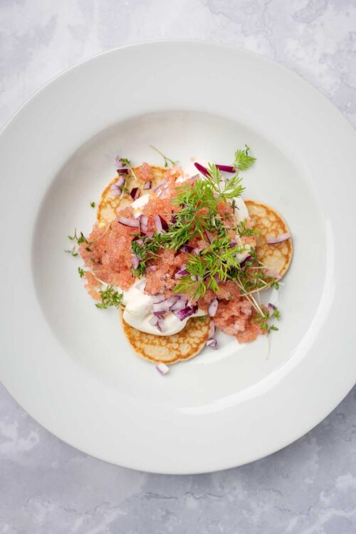 Overhead view of bowl of lumpfish caviar served with blinis.