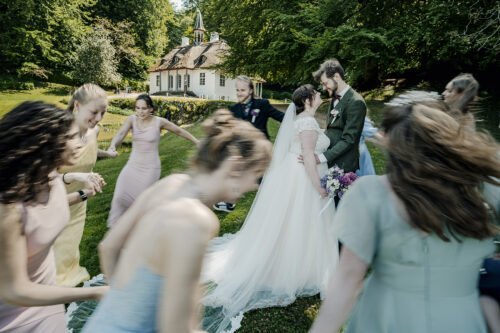 Brudepar omkranset af dansende gæster foran Det Hvide Hus i Liselund Slotspark på Møn – bryllupsfotografering.